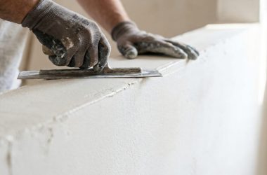 a person wearing gloves is smoothing plaster on a wall with a trowel indoors.