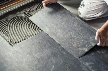 worker placing dark grey ceramic floor tiles on adhesive surface